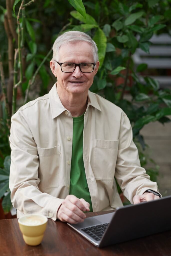 Elderly man enjoying remote work on a laptop in a garden setting.